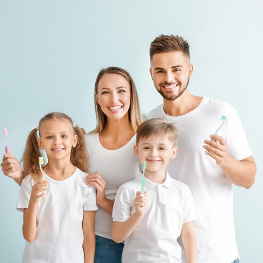 a family smiling while holding toothbrushes in Arlington
