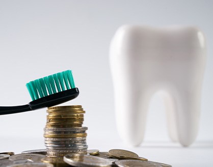 Toothbrush on a stack of coins with dental implant crown in the background